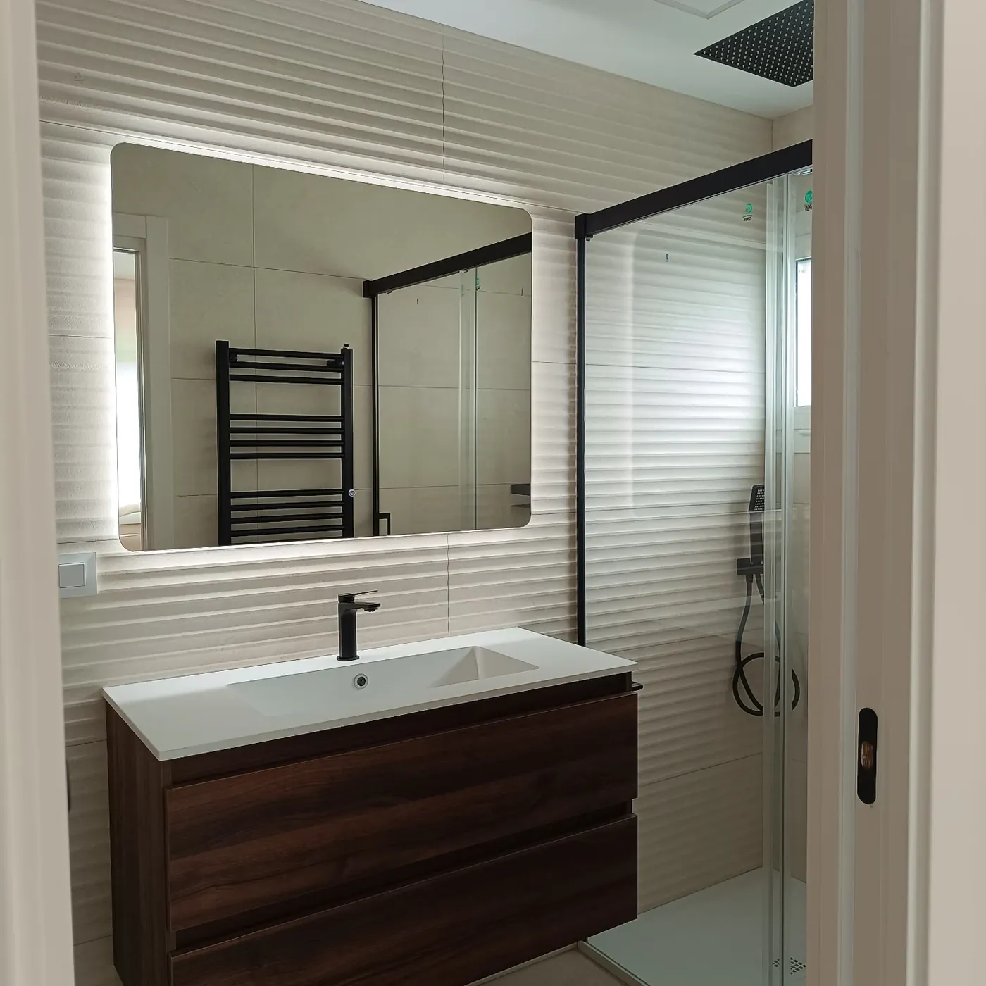 Baño con espejo retroiluminado, mueble de nogal y mampara