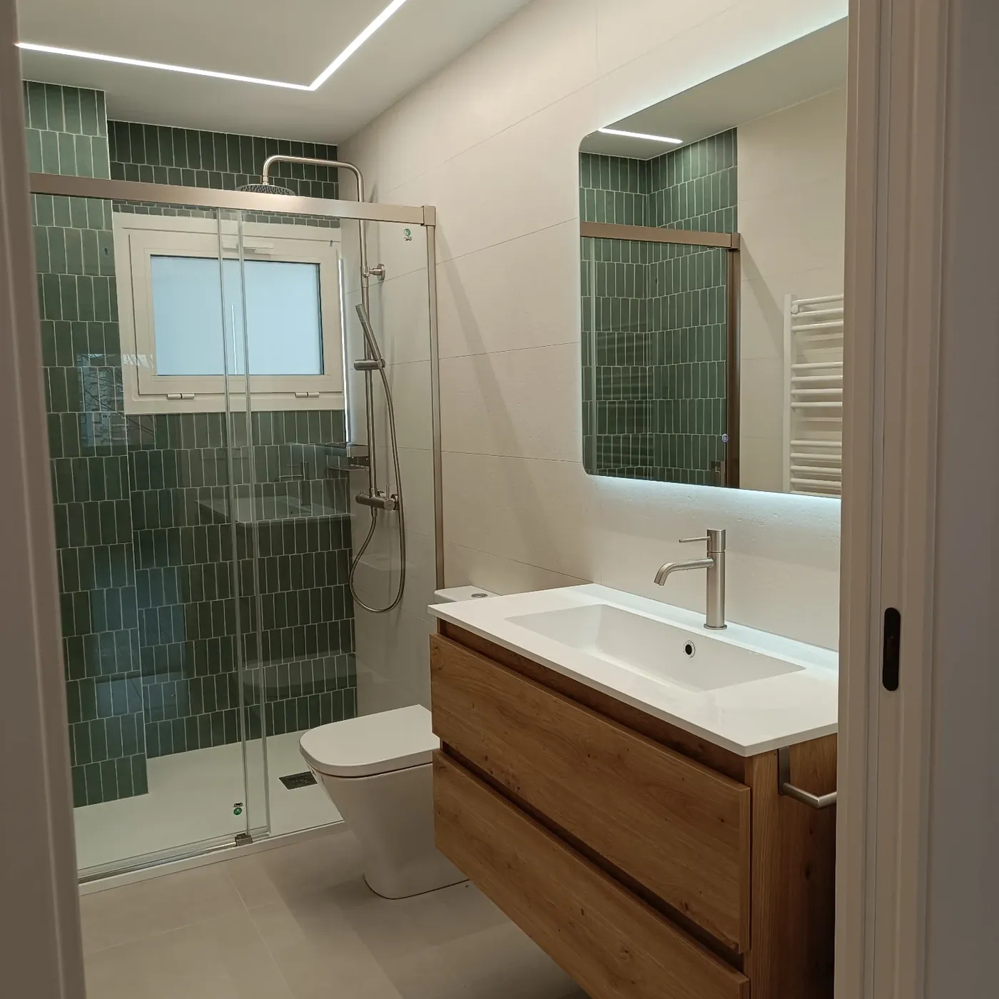 Baño con azulejo verde a media altura y lavabo sobre mueble de madera