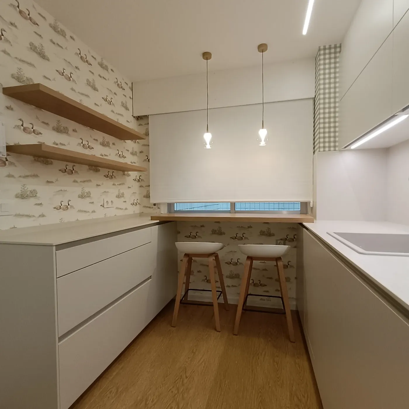Cocina reformada con barra de madera bajo la ventana y papel pintado